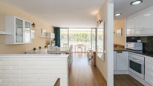 Una cocina moderna con armarios blancos, un comedor con mesa y sillas, y vistas a un balcón con plantas.