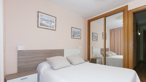 Un dormitorio con una cama, dos mesitas de noche, un tocador, un espejo y una puerta con espejo corredera.