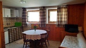 A compact kitchen with a dining table and chairs, a small television, and a sofa.