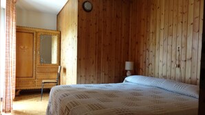 A wooden-paneled room with a bed, a chair, a wardrobe, and a lamp.