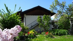 A house with a sloped roof, a staircase leading to an upper level, and a well-maintained garden with various flowers and greenery.