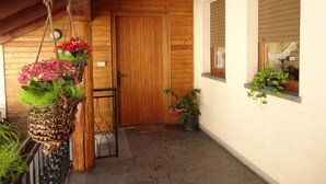 A wooden door with a small window, a hanging plant with red flowers, and a potted plant on the wall.