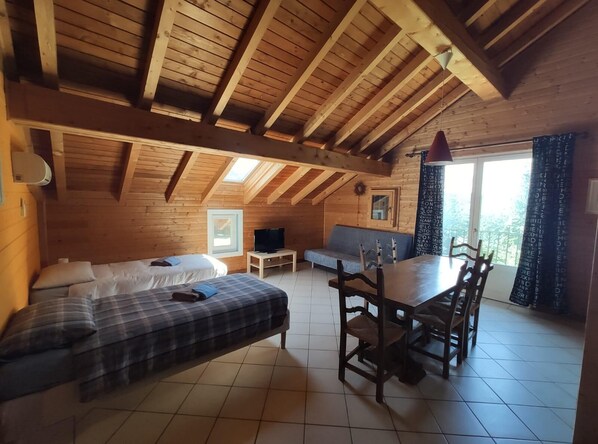 Une chambre confortable située dans les combles, avec un lit, une télévision, un canapé et une table à manger avec des chaises.