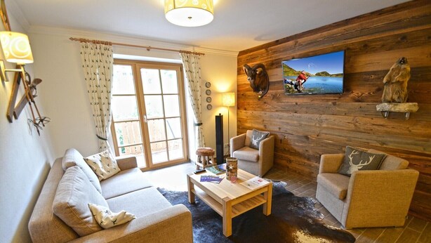 A cozy living room with a sofa, two armchairs, a coffee table, and a TV mounted on a wooden wall.