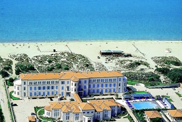 A large hotel with multiple buildings, a swimming pool, and a beach in the background.