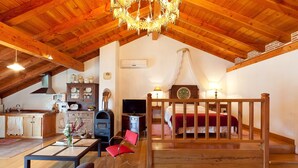 Ein gemütliches Zimmer mit Holzbalkendecke, einem Bett mit Baldachin, einem Essbereich mit Tisch und Stühlen sowie einer Küchenzeile mit Schränken und einem Herd.
