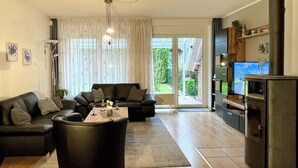 A living room with a sofa, coffee table, and a television. There is a sliding glass door leading to a balcony. - Generous and tasteful: This terraced house of about (Carolinensiel)