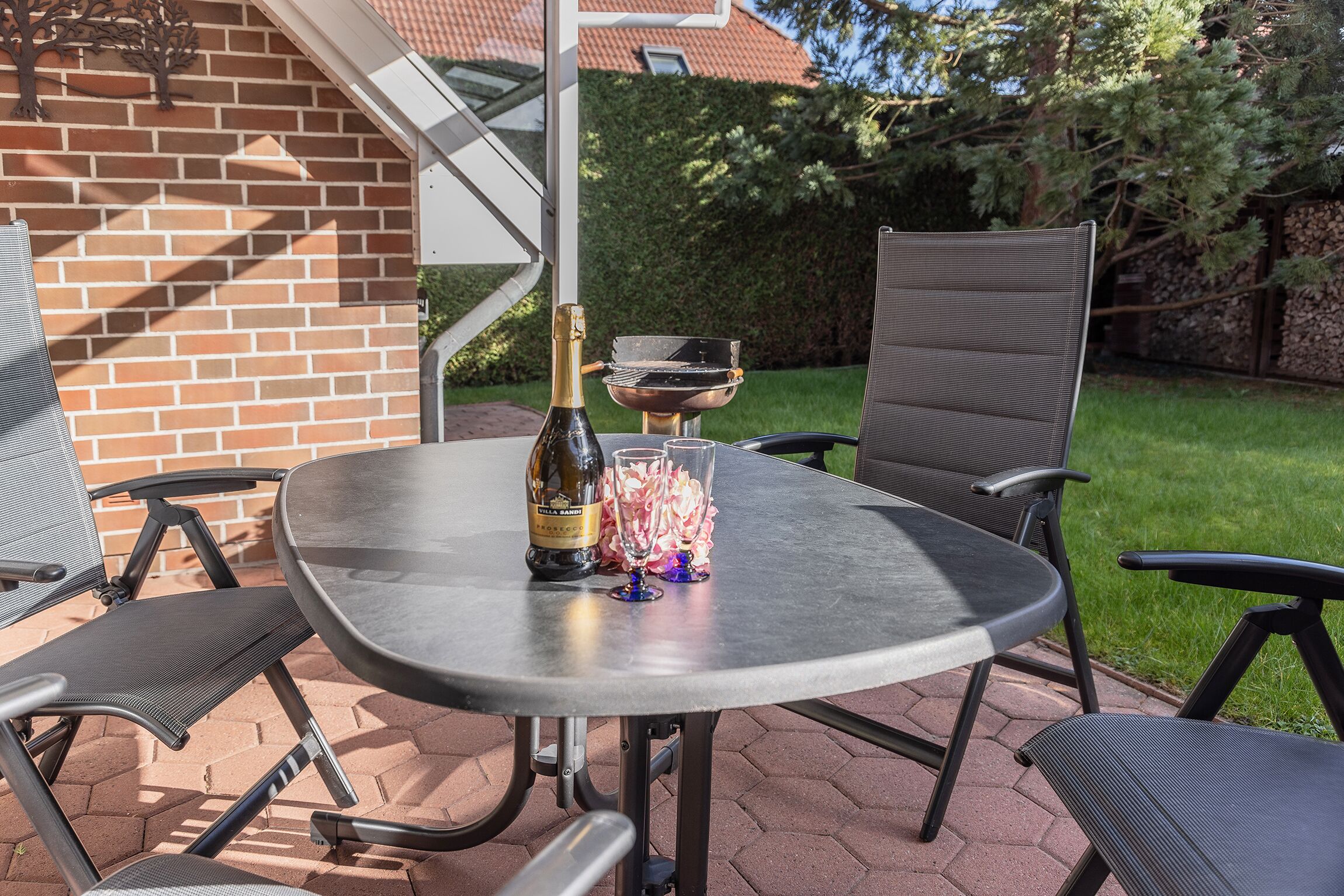 An outdoor patio with a metal table and chairs, a bottle of champagne, and a glass.