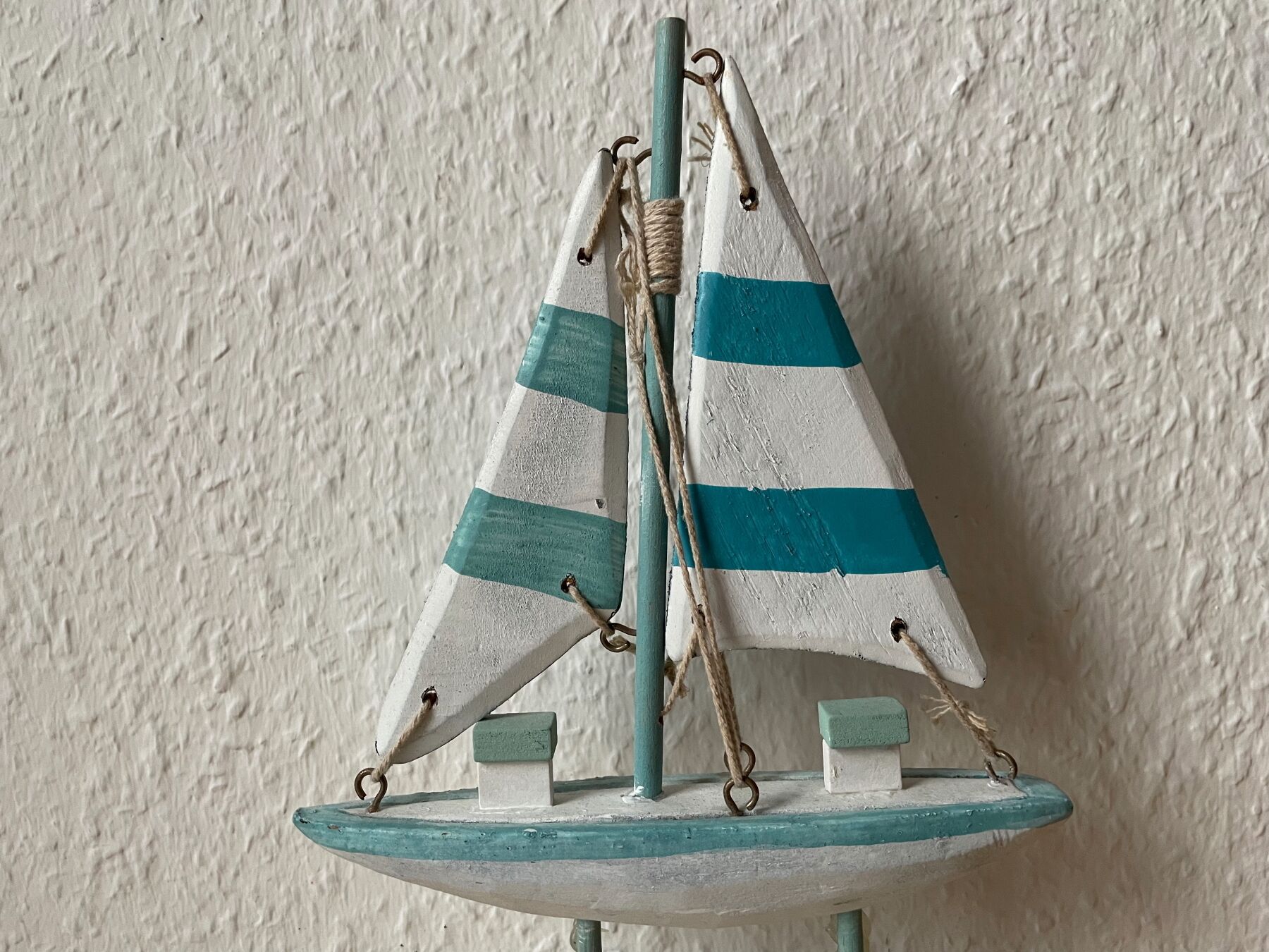 A small sailboat model with teal and white stripes, mounted on a teal base.