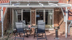 A patio with two black chairs and a table, a grill, and a glass door leading to an interior space. - Generous and tasteful: This terraced house of about (Carolinensiel)