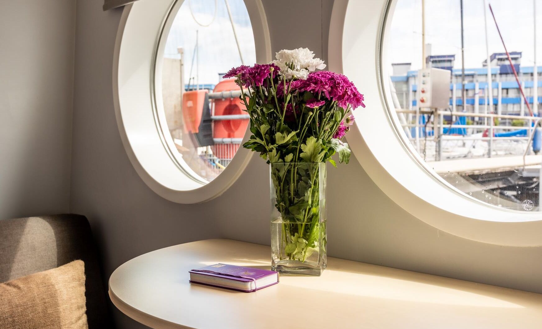 Una habitación con una mesa redonda, un libro morado y un jarrón con flores.