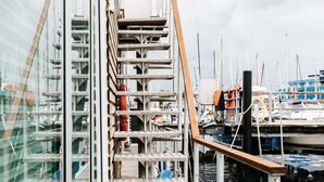 A multi-level wooden deck with metal railings, surrounded by water and docked boats. - Houseboat Canoga in Labo marina (Laboe)
