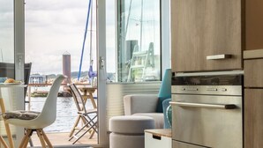 A modern kitchen with stainless steel appliances, a wooden cabinet, and a view of the water outside. - Houseboat Canoga in Labo marina (Laboe)