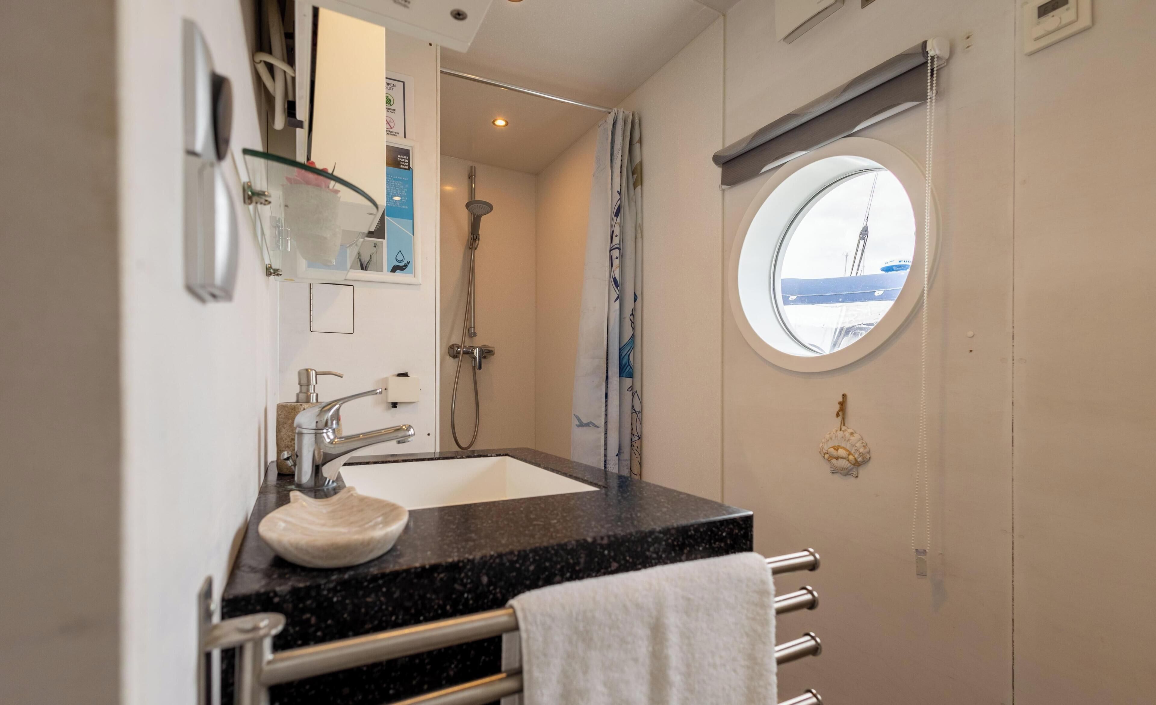 Een badkamer met een wastafel, spiegel, douche en een raam met uitzicht.
