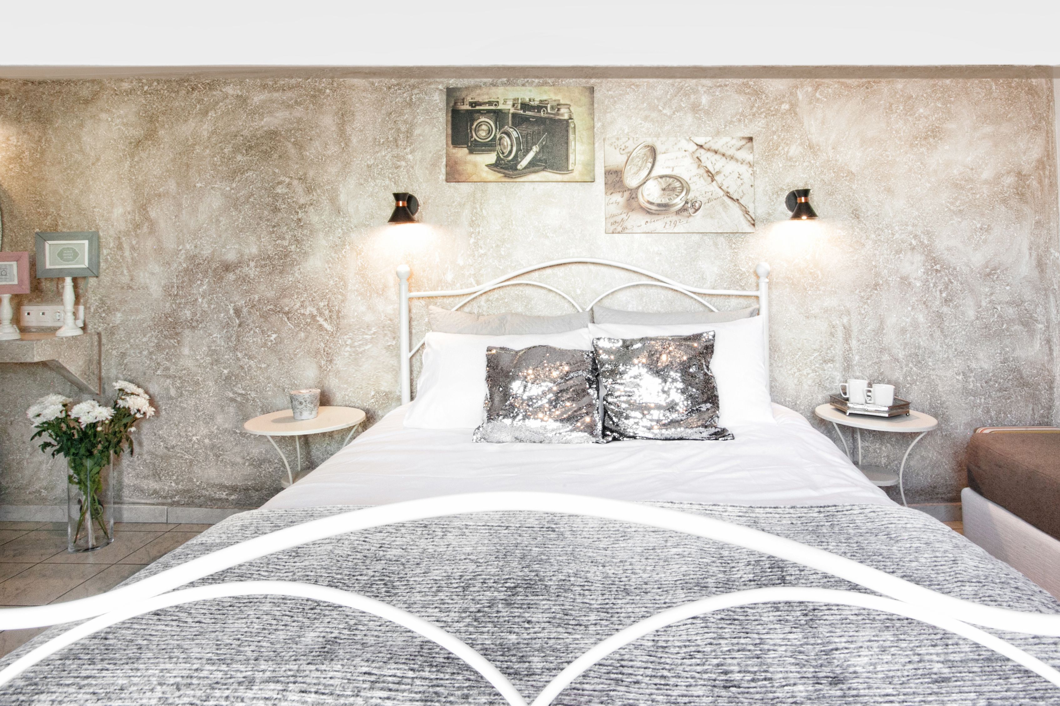 Une chambre moderne avec un grand lit, deux tables de chevet, une commode, un mur décoratif et une petite table sur laquelle est posé un vase de fleurs.