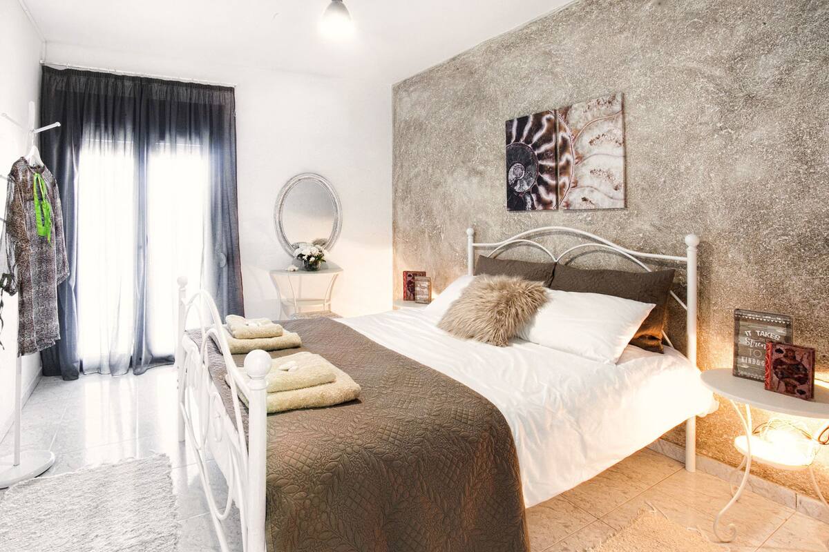 A bedroom with a bed, a bedside table, a mirror, and a wall with a textured pattern.