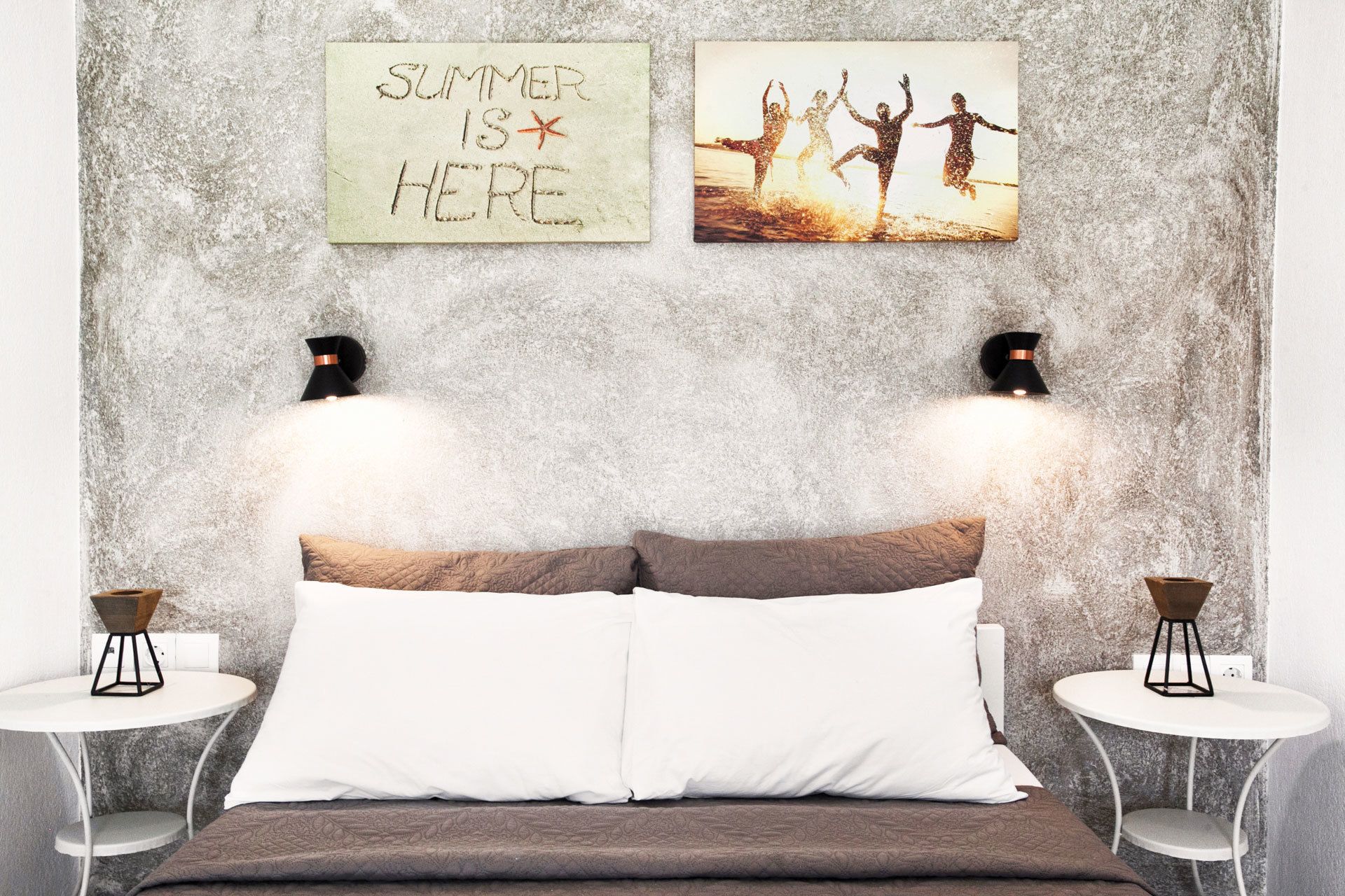 A bedroom with a bed, two bedside tables, a wall-mounted light fixture, and two wall decorations.