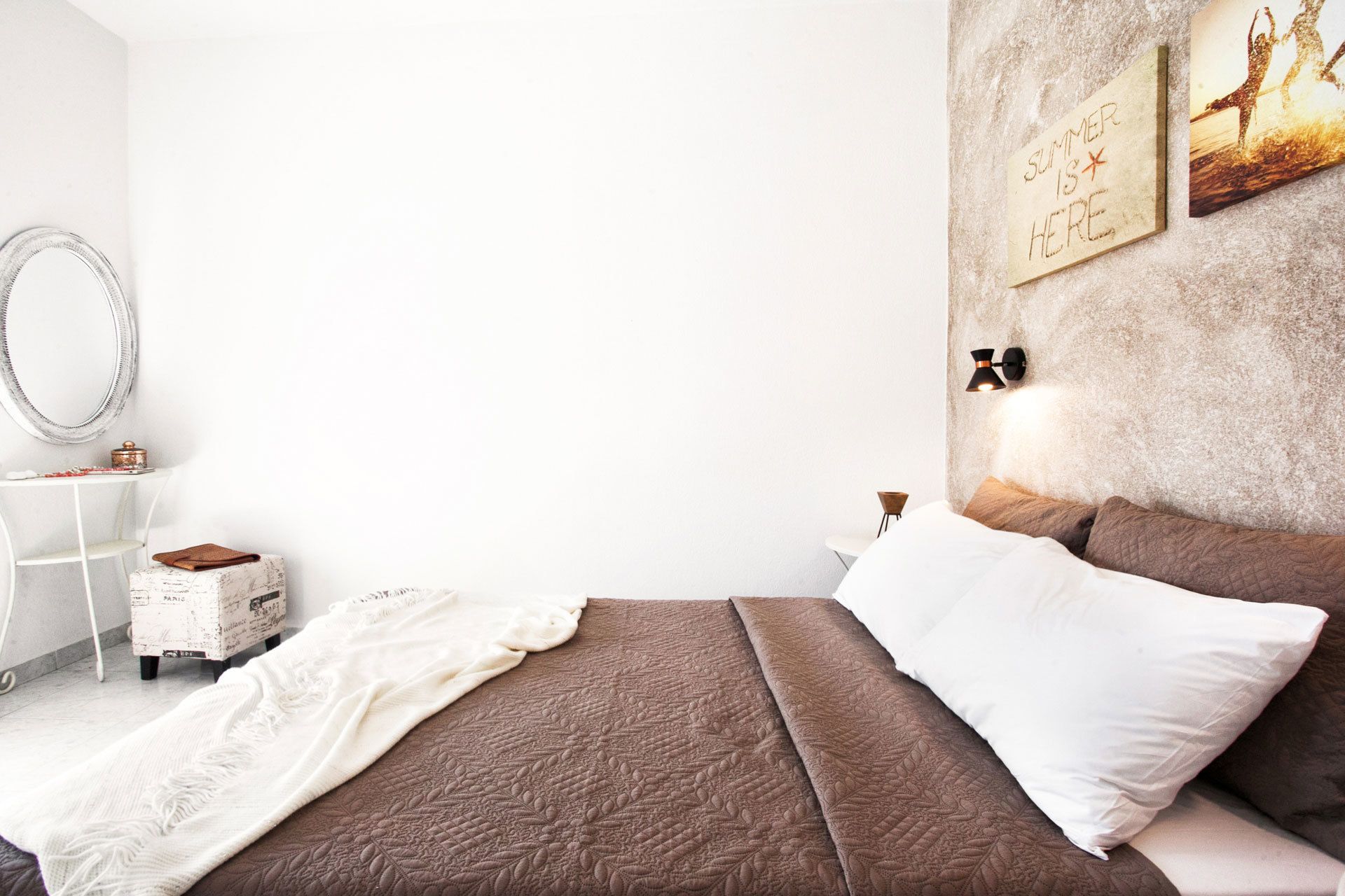 A bedroom with a bed, a nightstand, a mirror, and a wall-mounted light fixture.