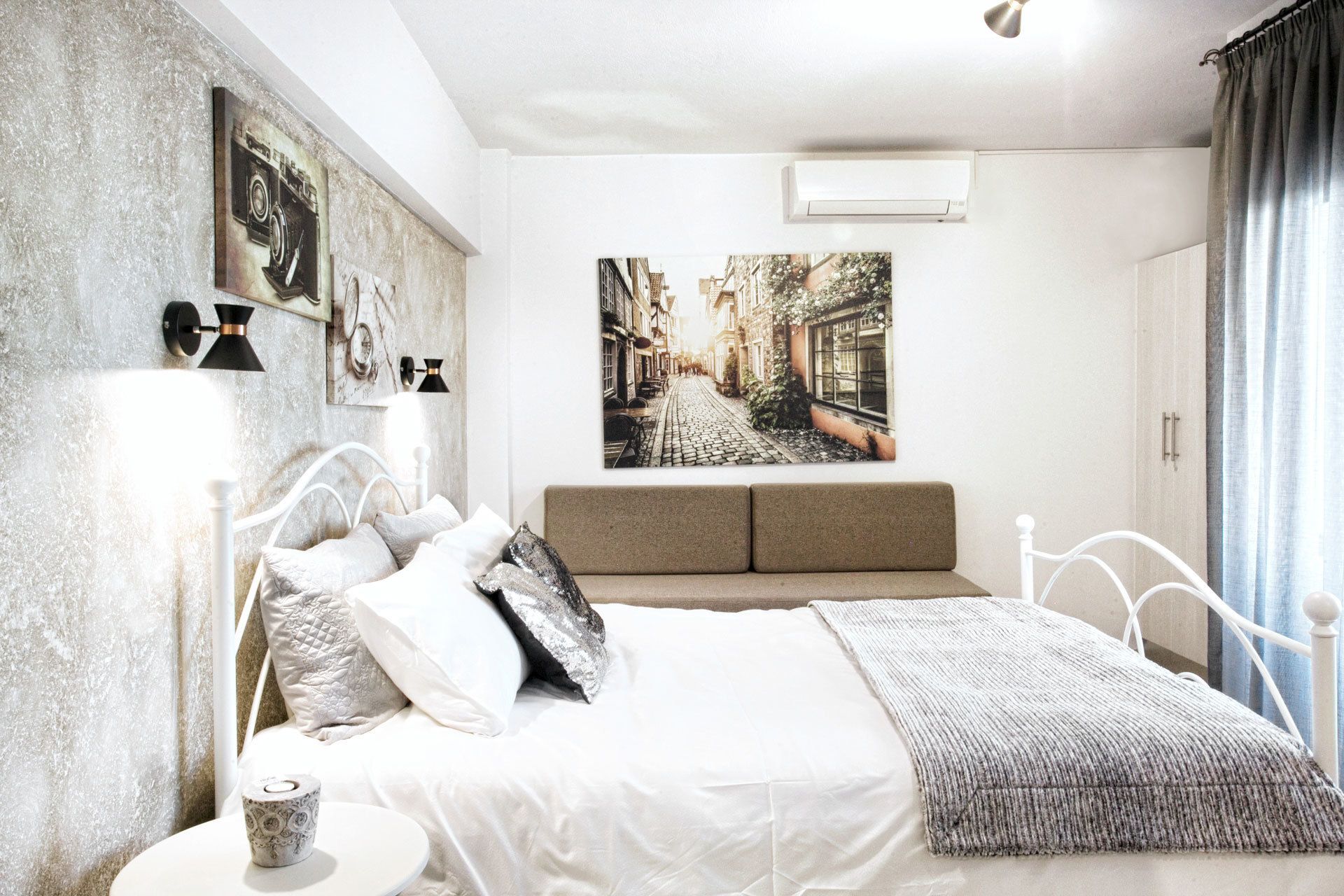 A bedroom with a bed, a bedside table, a lamp, a picture on the wall, and a window with curtains.