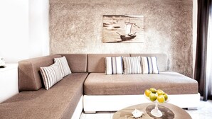 A modern living room with a brown sectional sofa, striped pillows, a round coffee table with a fruit bowl, and a maritime-themed painting on the wall. - Asprolithos Studios (Skiathos)