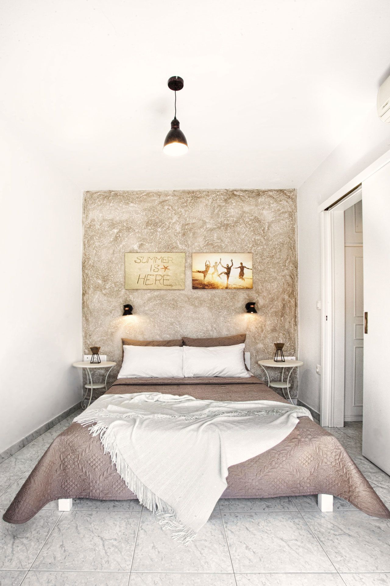 A bedroom with a large bed, a headboard with a textured wall, two bedside tables with lamps, and a door to the right.