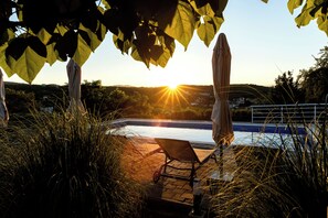 A poolside area with a chair and umbrella, surrounded by greenery and a view of the sunset over the water. - Family destination (Zmijavci)