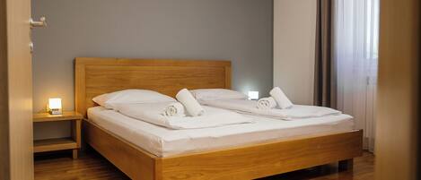 A neatly made bed with white linens and towels, a wooden headboard, a bedside table with a lamp, and an air conditioning unit on the wall.