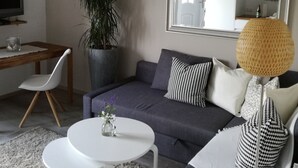 Sala de estar con sofá gris, mesa de centro blanca y un espejo grande. Hay una planta en maceta y una lámpara en el suelo.