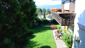 Un jardín con terraza de madera, una banca y una mesa adornada con flores.