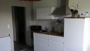 Una cocina moderna con armarios blancos, encimera de madera y microondas integrado. Hay una pequeña mesa con mantel blanco y un jarrón con flores.
