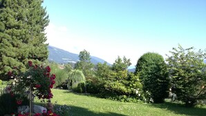 Un jardín bien cuidado con diversas plantas y flores, un sendero pavimentado y vistas a montañas distantes.