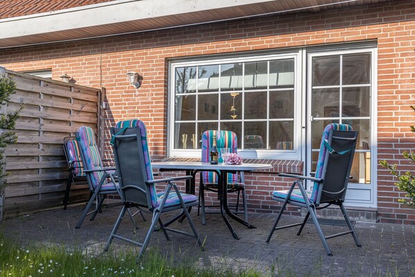 A patio with four chairs and a table, a brick wall, and a large window. - Time unwind: The townhouse is located behind the dike and has for d (Harlesiel)