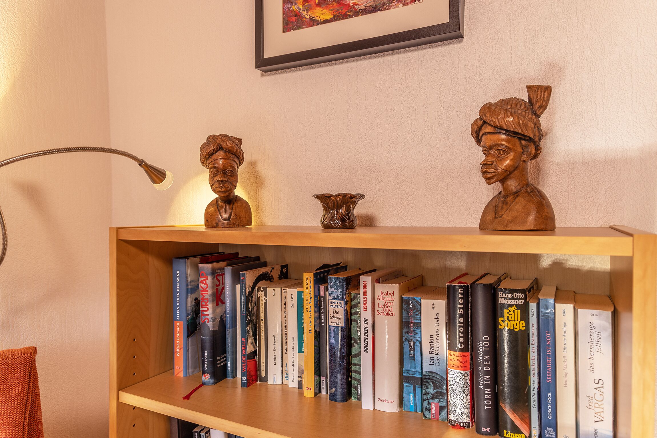 Una estantería con varios libros y dos esculturas de madera.