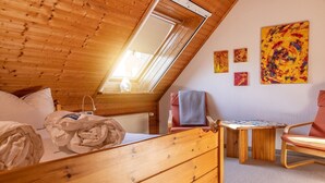 Un dormitorio acogedor en el ático, con techo inclinado, muebles de madera, un tragaluz y obras de arte en las paredes.