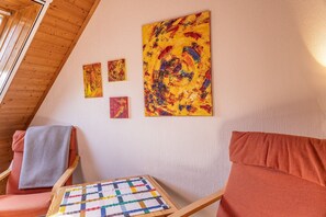 Tunnelmallinen huone, jossa on puupalkit katossa, punainen sohva, harmaa nojatuoli ja pienellä pöydällä peitto.