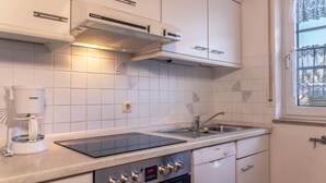 Una cocina moderna con armarios blancos, estufa integrada, cafetera y una ventana con encaje decorativo.