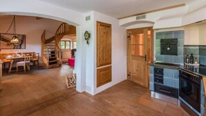 A spacious kitchen with modern appliances, a wooden staircase, and a dining area with a wooden table and chairs. - Farmhouse Tegernsee (Warngau)