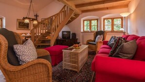 A cozy living room with a wooden staircase, a red sofa, wicker chairs, and a small table with fruit. - Farmhouse Tegernsee (Warngau)
