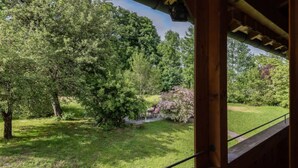 A view of a lush garden with trees and a small pond, visible through a wooden structure with a railing. - Farmhouse Tegernsee (Warngau)