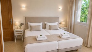 Una cama doble con dos almohadas, una mesita de noche con lámpara y una ventana con cortinas.