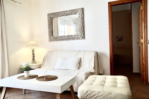 Een kamer met een bed, een witte tafel met een lamp, een spiegel en een deur.