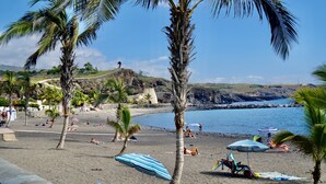 A beach with palm trees, umbrellas, and people relaxing. - Playa San Juan, 2 room apartment close to the beach me WiFi (Playa San Juan)