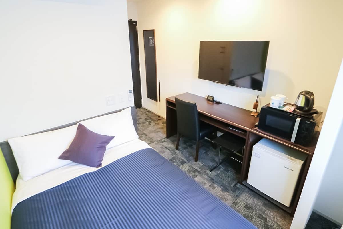 Ein Hotelzimmer mit Bett, Schreibtisch, Fernseher, Kaffeemaschine und kleinem Kühlschrank.
