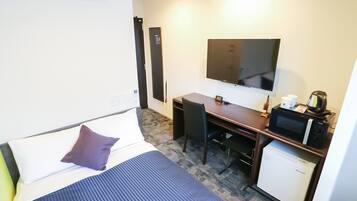Habitación de hotel con cama, escritorio, televisor, cafetera y refrigerador pequeño.