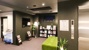 Eine Hotelhalle mit einer gepolsterten grünen Sitzecke, einem Empfangstresen, einem Live-TV-Bildschirm und einer Wand mit einer Speisekarte.