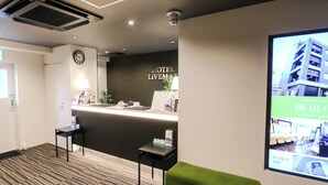 Ein Hotel-Rezeptionsbereich mit Empfangstresen, einer Uhr und einem digitalen Bildschirm, der Hotelinformationen anzeigt.