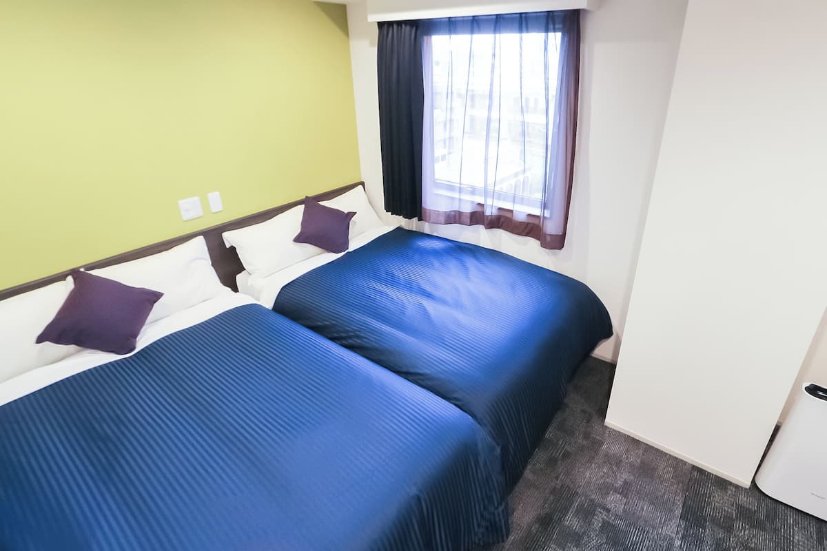 Ein Hotelzimmer mit zwei Betten, einem fensterbelaubten Fenster und einer grünen Wand.