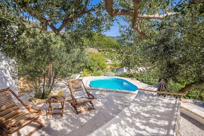 A pool area with a wooden deck, lounge chairs, and a view of a hillside.
