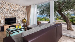 A living room with a stone wall, a television, a globe, and a view of the outdoors. - Private pool family home with open sea view (Bol)