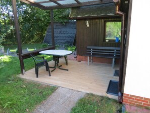 A covered patio with a table and chairs, a bench, and a wooden structure with a window. - "Ferienhaus Antje" directly on the river, Spreewaldhof Schupan in Burg (Spreewald) (Burg (Spreewald))